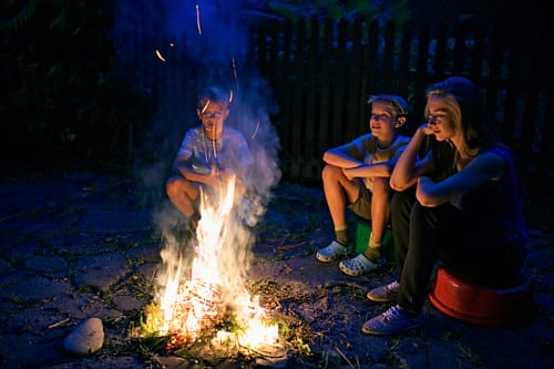 Three kids enjoying a small bonfire in backyard