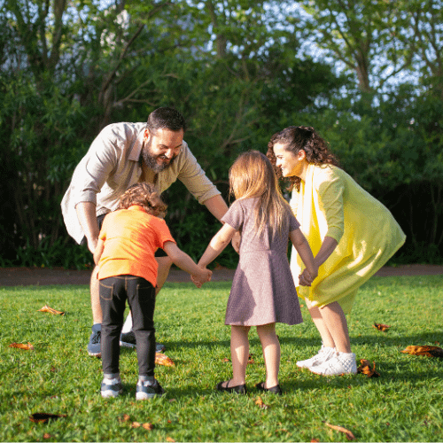 Family of 4, mom and dad playing outside with younger son and daughter holding hands.